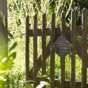 Holzzaun mit einem Schild im Garten des Klinikum Schloss Lütgenhof, der die harmonische Verbindung zur Natur zeigt.