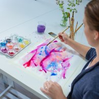 Eine Frau malt mit Farben auf einem Tisch, während sie sich in der Zeichentherapie entspannt und kreativ ausdrückt.