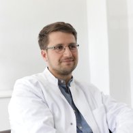 Ein Mann mit Brille sitzt entspannt in einem Stuhl, Dr. med. et phil. Christian Schmidt, nachdenklich und konzentriert.