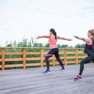 Zwei Frauen praktizieren Yoga auf einem Holzdeck, umgeben von Natur, im Rahmen einer Sporttherapie.